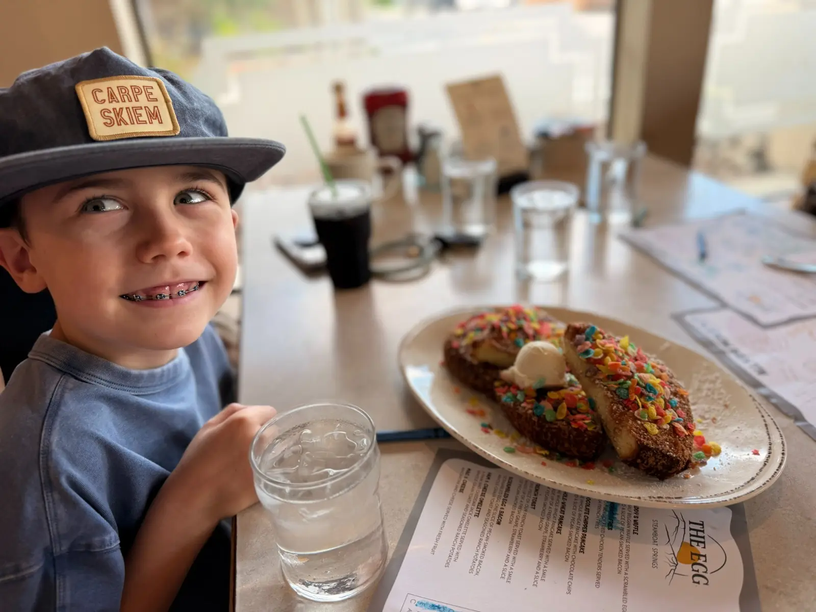 A child seated beside Fruity Pebbles French Toast at The Egg